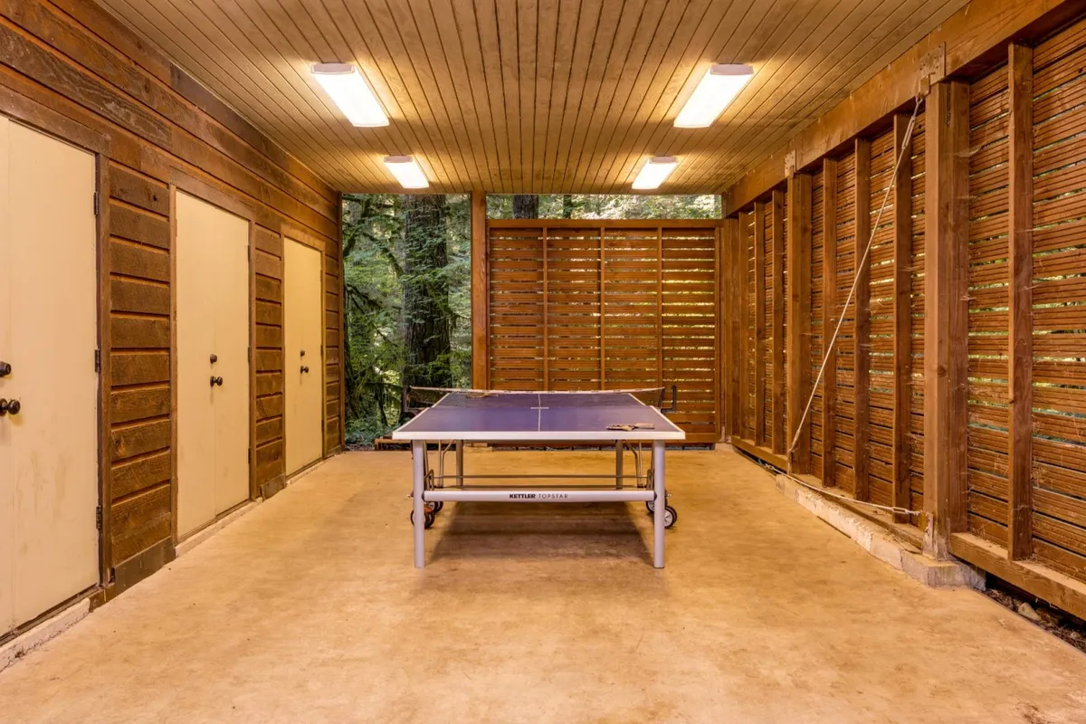 Inside a covered garage, a ping pong table stands ready for spirited matches. Wooden doors and slatted walls provide a rustic backdrop, creating a casual, playful environment for friendly family tournaments and indoor fun away from screens.