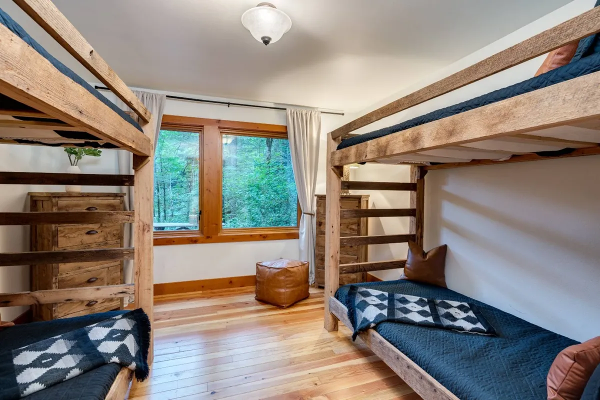 An inviting interior scene featuring cozy bunk beds beside a large window, with soft natural light and wooden furniture. The playful arrangement of bedding and relaxed atmosphere suggest a perfect space for kids or friends to wind down after a day of adventure.